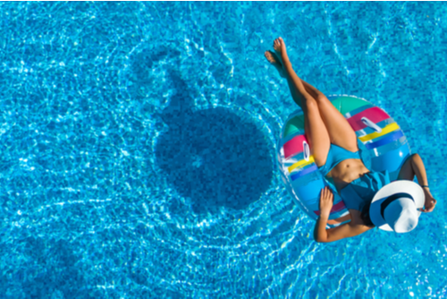 Aerial view of a slender woman wearing a white hat lying on an inner tube in the pool. 