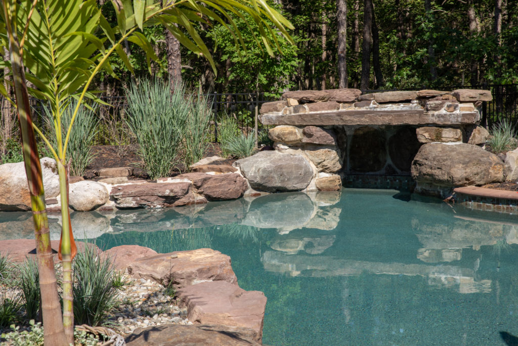 A rocky gunite pool with a grotto opening in a natural setting. 