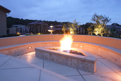 Triangle-shaped, lit concrete fire pit surrounded by concrete bench in home backyard. 