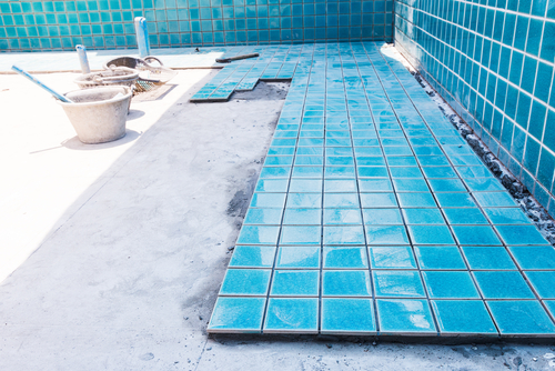 Blue tiling in the process of being installed on the floor of an in-ground pool. 