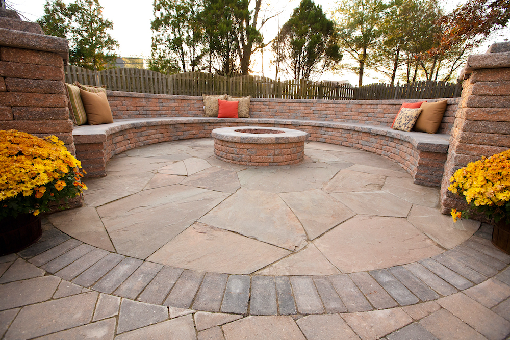 Brick floor leading to brick fire pit and long, concrete bench in backyard. 