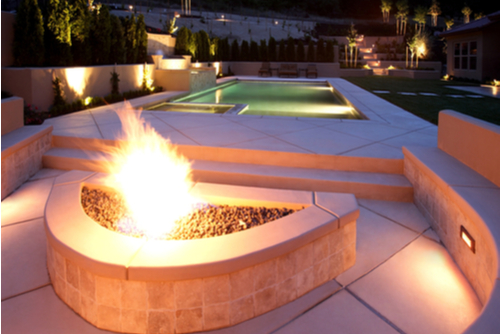 Small, rectangle in-ground luxury pool with an adjacent lit fire pit.