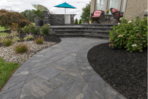 Gray paver pathway in backyard leading to deck. 