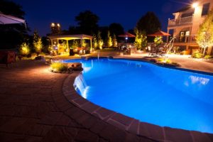 Home backyard at night featuring a custom inground pool and other outdoor living elements.